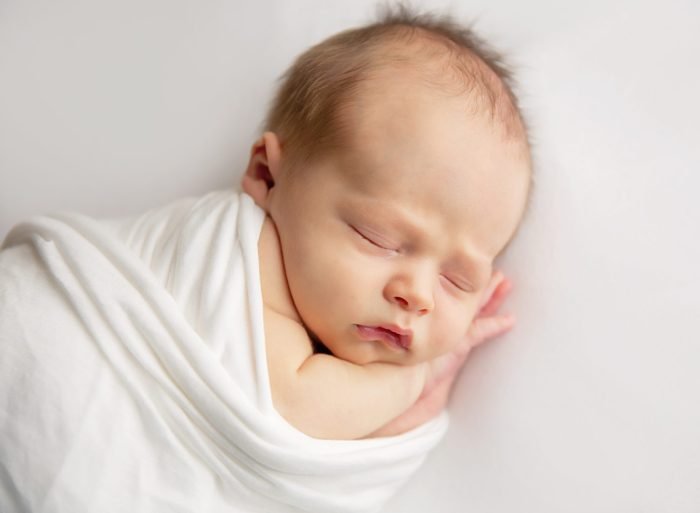 Newborn baby resting in parents’ arms during a New York City in-home photo session
