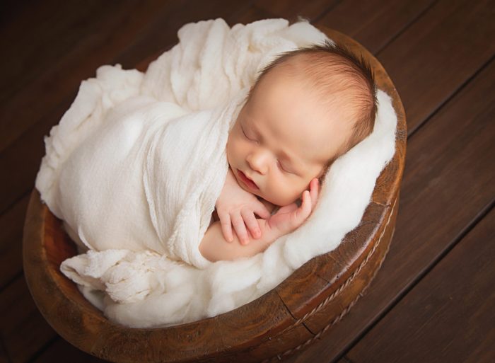 Newborn baby resting in parents’ arms during a New York City in-home photo session